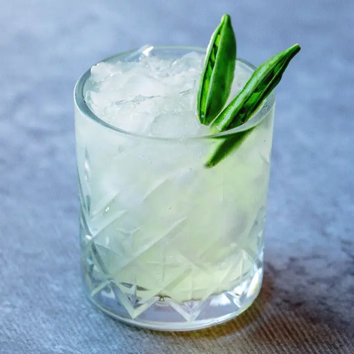 Green Giant cocktail in a crystal-cut rocks glass with ice, garnished with two sugar snap pea pods