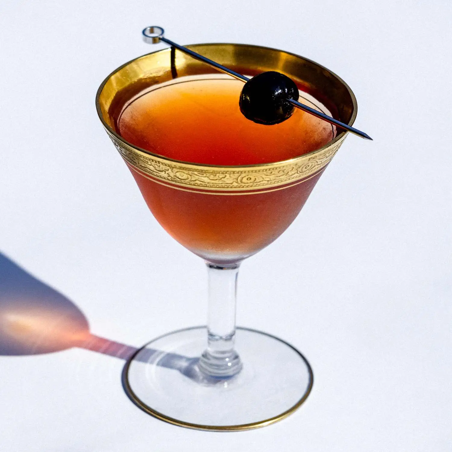 Boothby cocktail in ornate coupe glass with etched gold rim, garnished with maraschino cherry