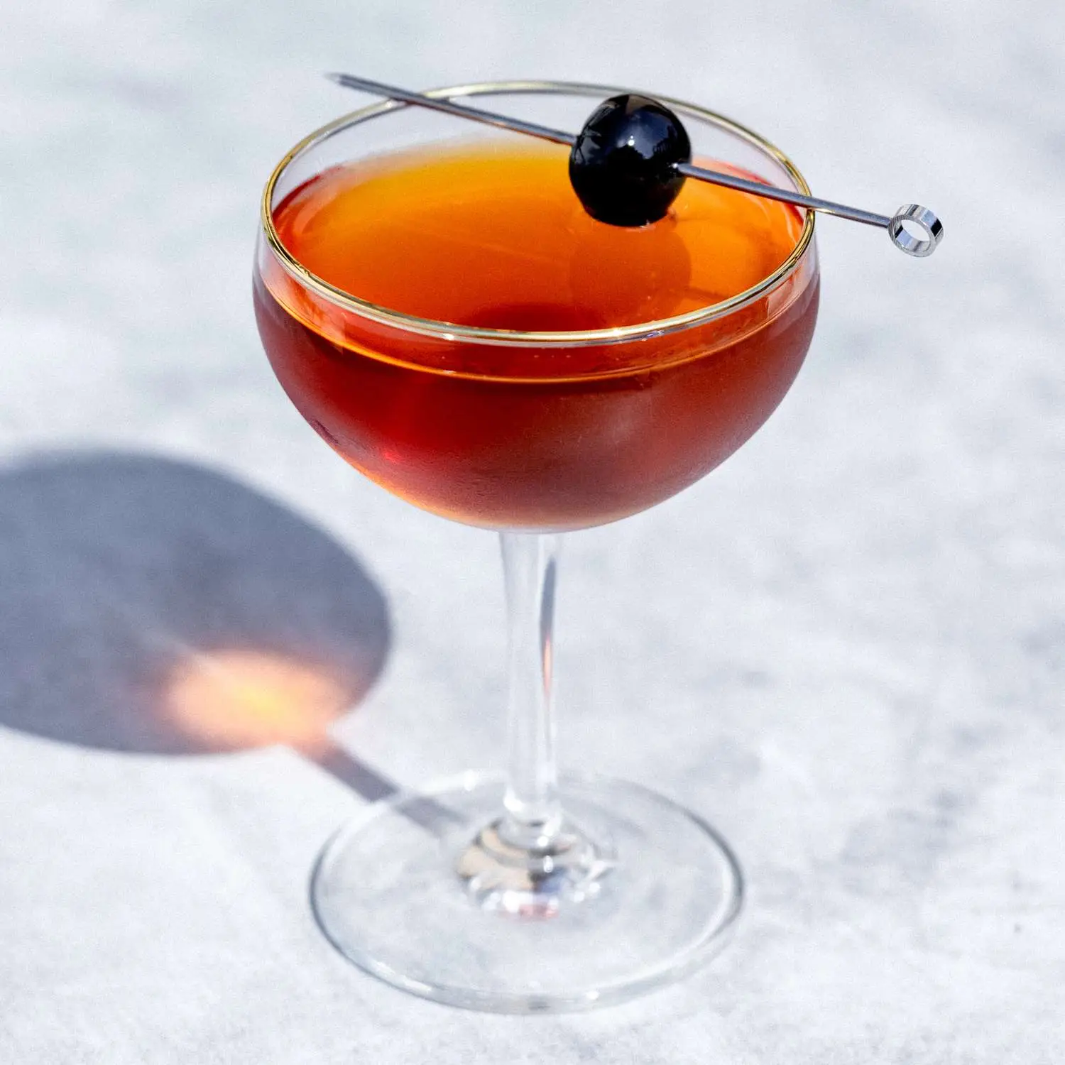 Manhattan cocktail in a curved coupe glass, with maraschino cherry garnish on a metal cocktail skewer