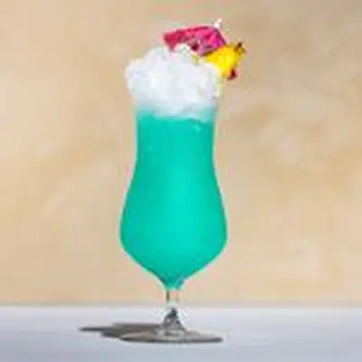 Blue Hawaii cocktail, bright teal and served over crushed ice in a curved Hurricane glass, garnished with a pineapple wedge and miniature red umbrella