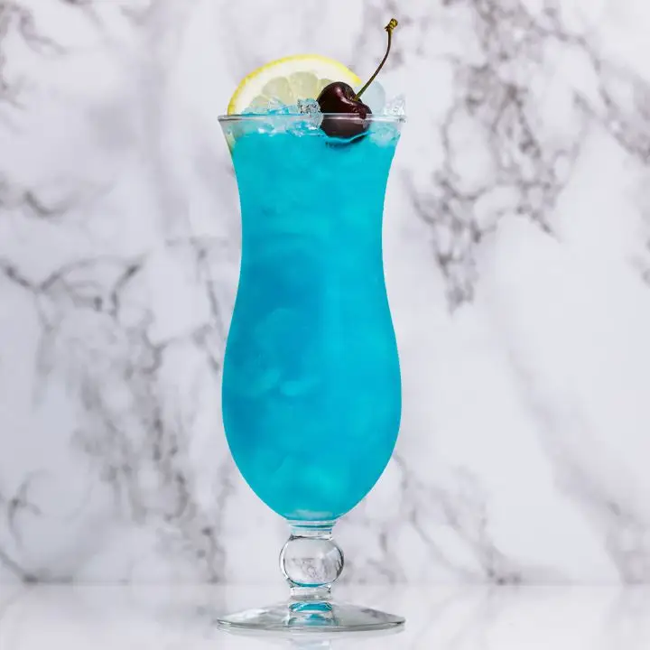 blue lagoon cocktail on a marble surface, garnished with a lemon and cherry