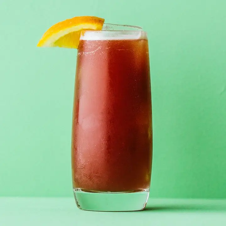 alabama slammer cocktail with orange garnish and green background