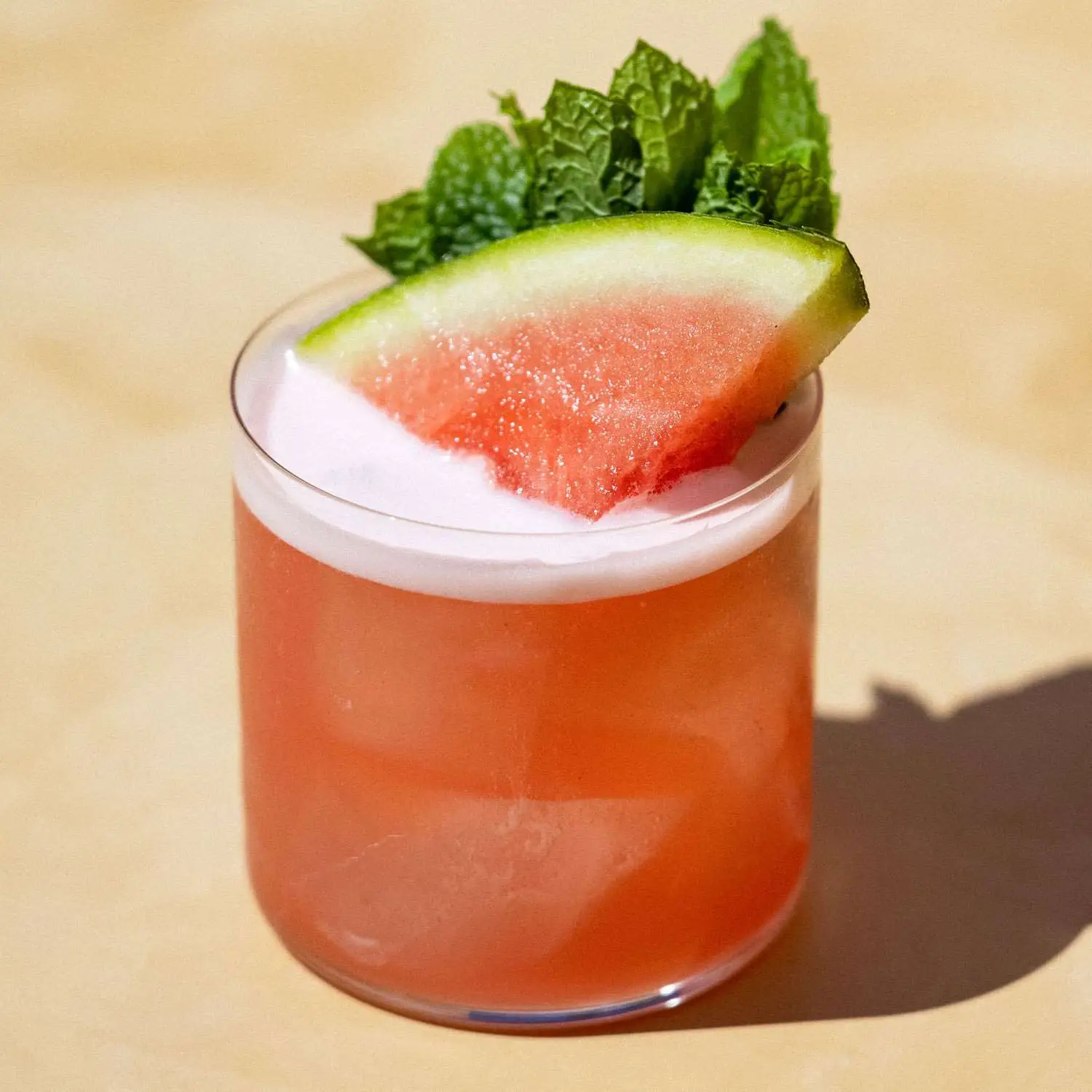 Red-pink watermelon Margarita in a rocks glass with watermelon wedge and mint spring garnish on top