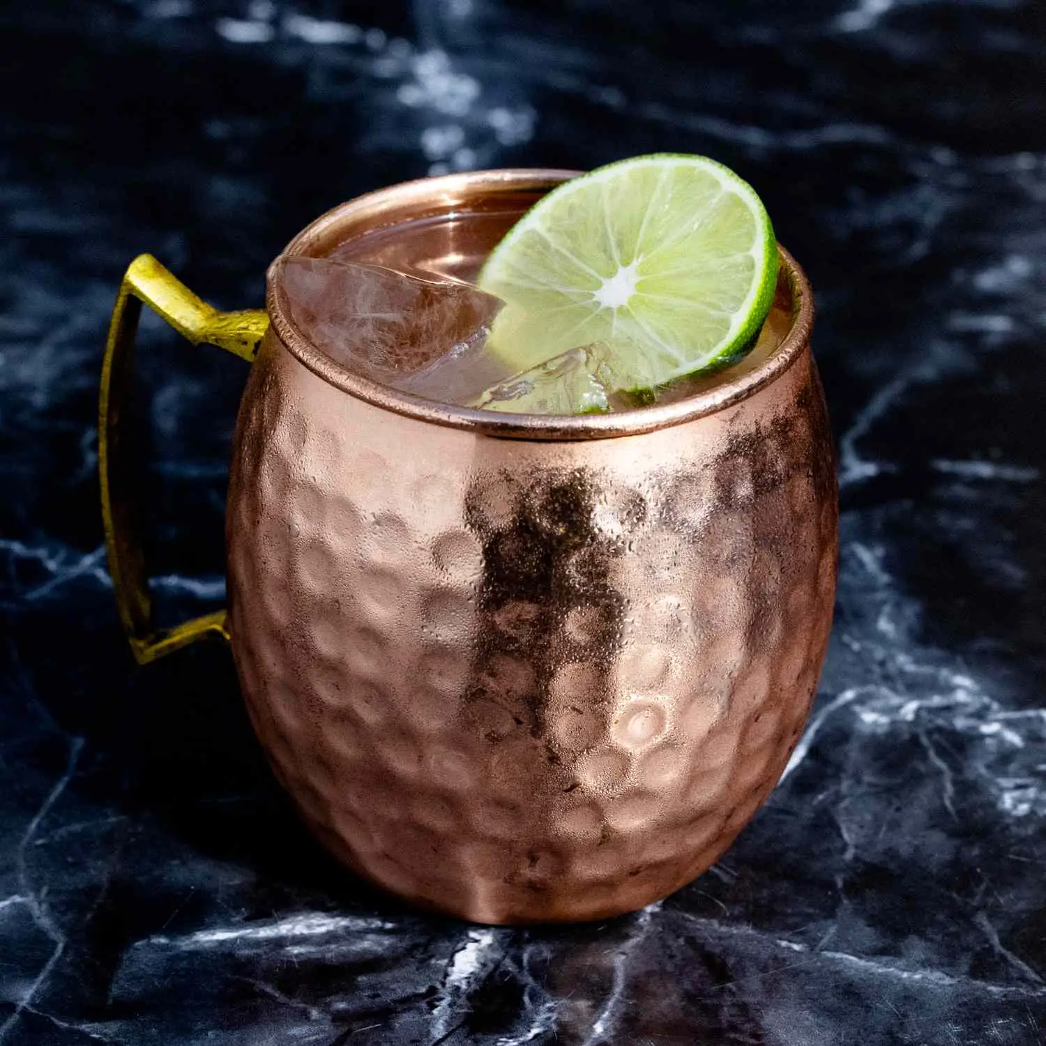 Moscow Mule in copper mug with small divots and lime wheel garnish, on dark marble background