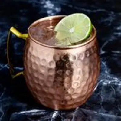 Moscow Mule in copper mug with small divots and lime wheel garnish, on dark marble background