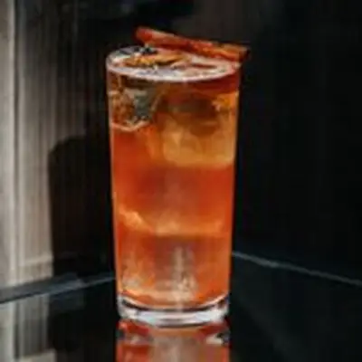 reddish-brown Ruby Hearts cocktail in a Collins glass, garnished with a cinnamon stick balanced on the rim of the glass