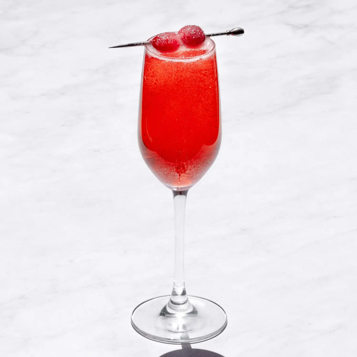 Red Cranberry Ginger Mimosa in flute glass with speared sugared cranberries on marble surface