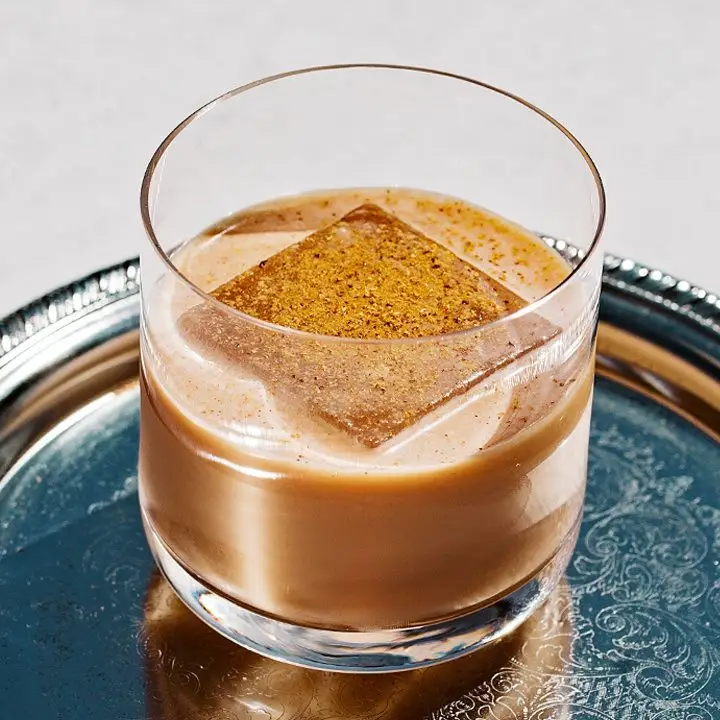 A silver bar tray holds an Old Fashioned glass. The glass is filled with a creamy drink on a large ice cube, garnished with nutmeg.
