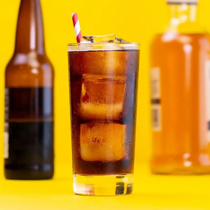 Bourbon and Root Beer cocktail on yellow surface with red-and-white straw