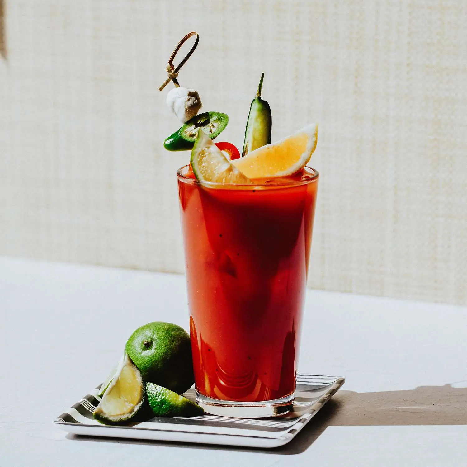 Bloody Maria on a striped coaster, garnished with citrus and peppers
