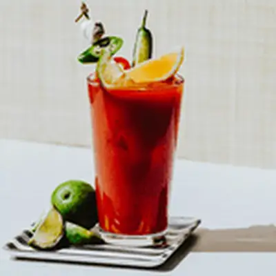 Bloody Mary in pint glass garnished with limes, parsley and olives, on silver tray surrounded by other garnishes