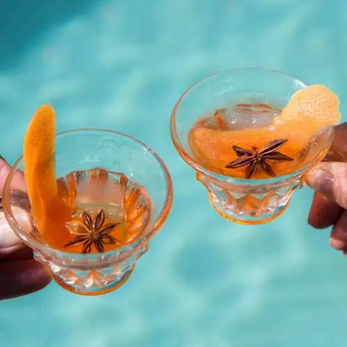 Two hands toast with Dizzy Blonde Negroni cocktails, served in punch glasses with grapefruit peel and star anise garnishes