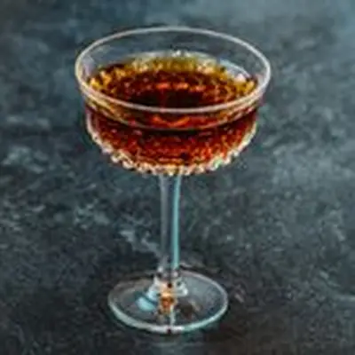 A deep red-brown stirred cocktail in an ornate stemmed cocktail glass against a dark gray background