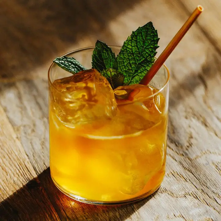 Whiskey Smash cocktail on ice with mint leaves and a straw