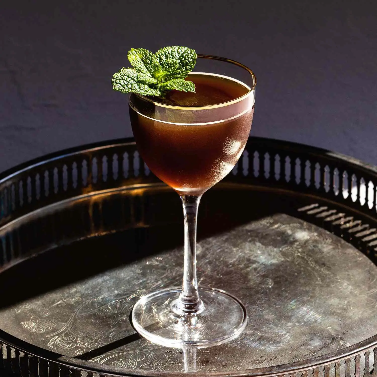 Death by Morning cocktail in gold-rimmed Nick & Nora class with mint sprig garnish, on metal serving tray