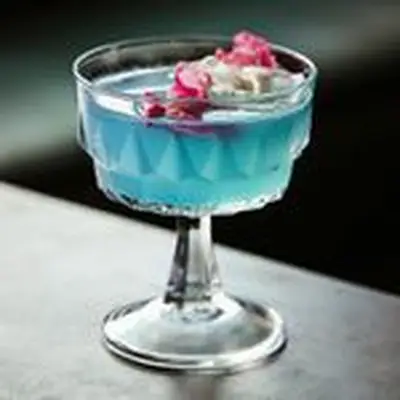 blue-colored Lady in Blue cocktail in a coupe, garnished with edible flowers