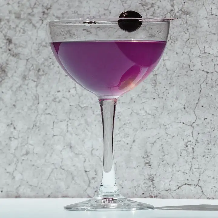 Purple-hued Aviation cocktail in a coupe with a cherry garnish
