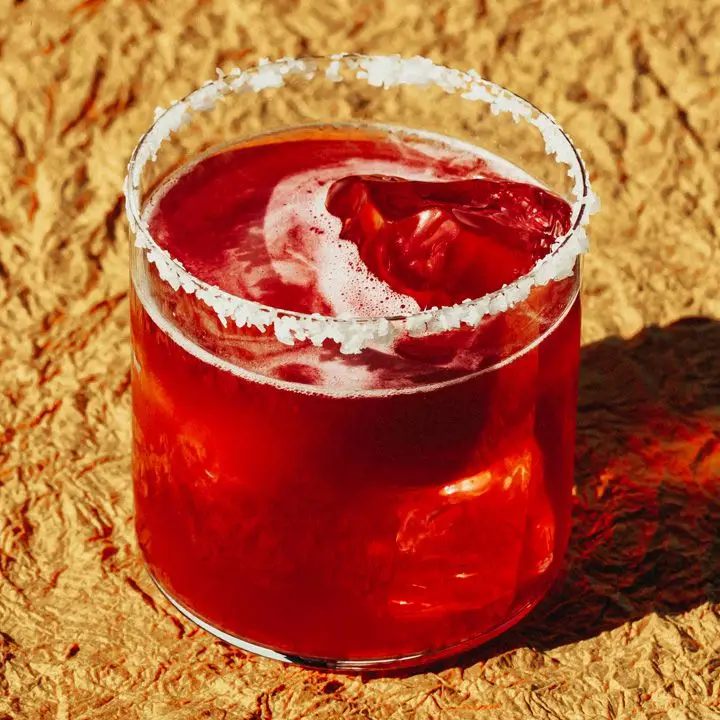 Reddish-purple Concord Grape Margarita on ice, served in a smoked salt-rimmed rocks glass