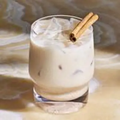 Coquito in rocks glass on tan marble countertop, with cinnamon stick garnish