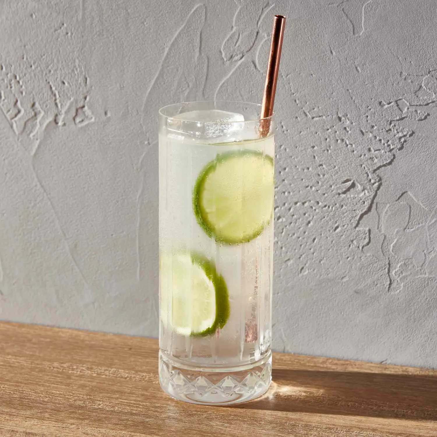 Gin Rickey with two lime wheels in highball glass with copper straw