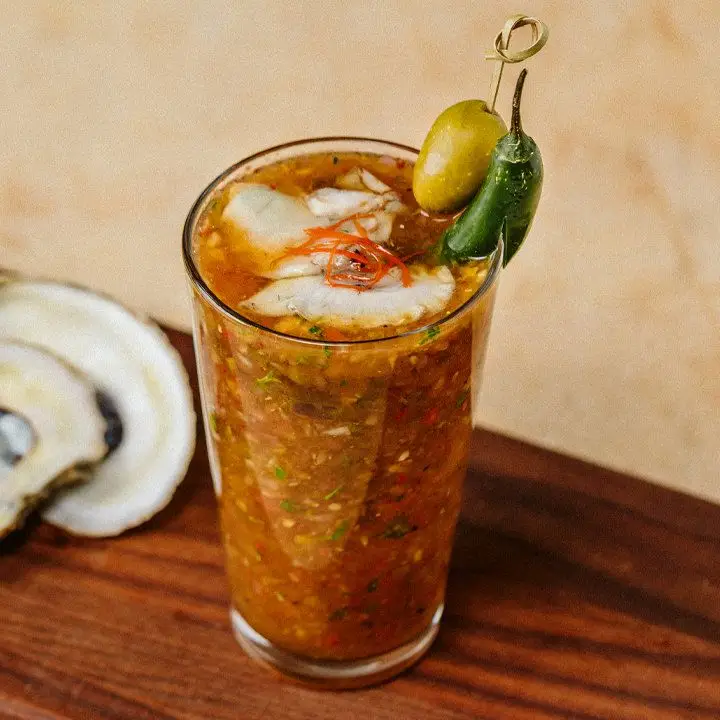 Bloody Roman cocktail in a pint glass, topped with two oysters, a green olive, serrano pepper and red chile threads