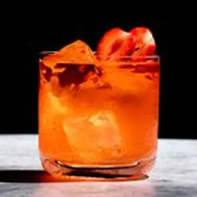 red-colored El Chapo cocktail in a rocks glass, garnished with two skewered strawberries slices 