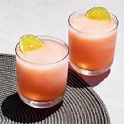 two Pink Frozen Margaritas in rocks glasses with lime wheels poking out of their tops