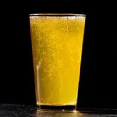 An effervescent, sunny-yellow beverage called Radler cocktail in a pint glass, made by combining beer and lemonade in the cup.