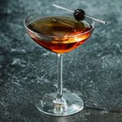 Red Hook cocktail in a cocktail glass with a skewered cherry balanced on the rim