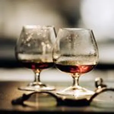 Two snifters of cognac pictures on a dark surface with a watch and ring scattered around.