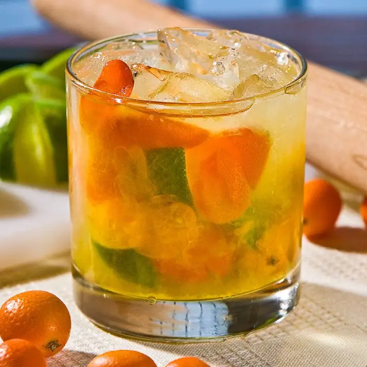 Honey Kumquat Caipirinha cocktail in a rocks glass, with muddled kumquats and limes in the glass