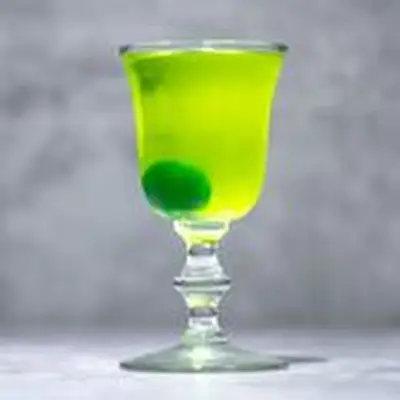 Neon green Greenhorn cocktail in Nick & Nora glass, with green maraschino cheery at bottom, on marble background
