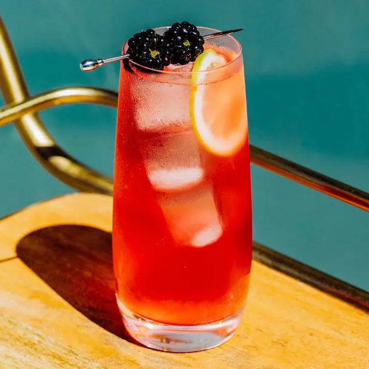 oaks lily cocktail garnished with two skewered blackberries, served on a bar cart