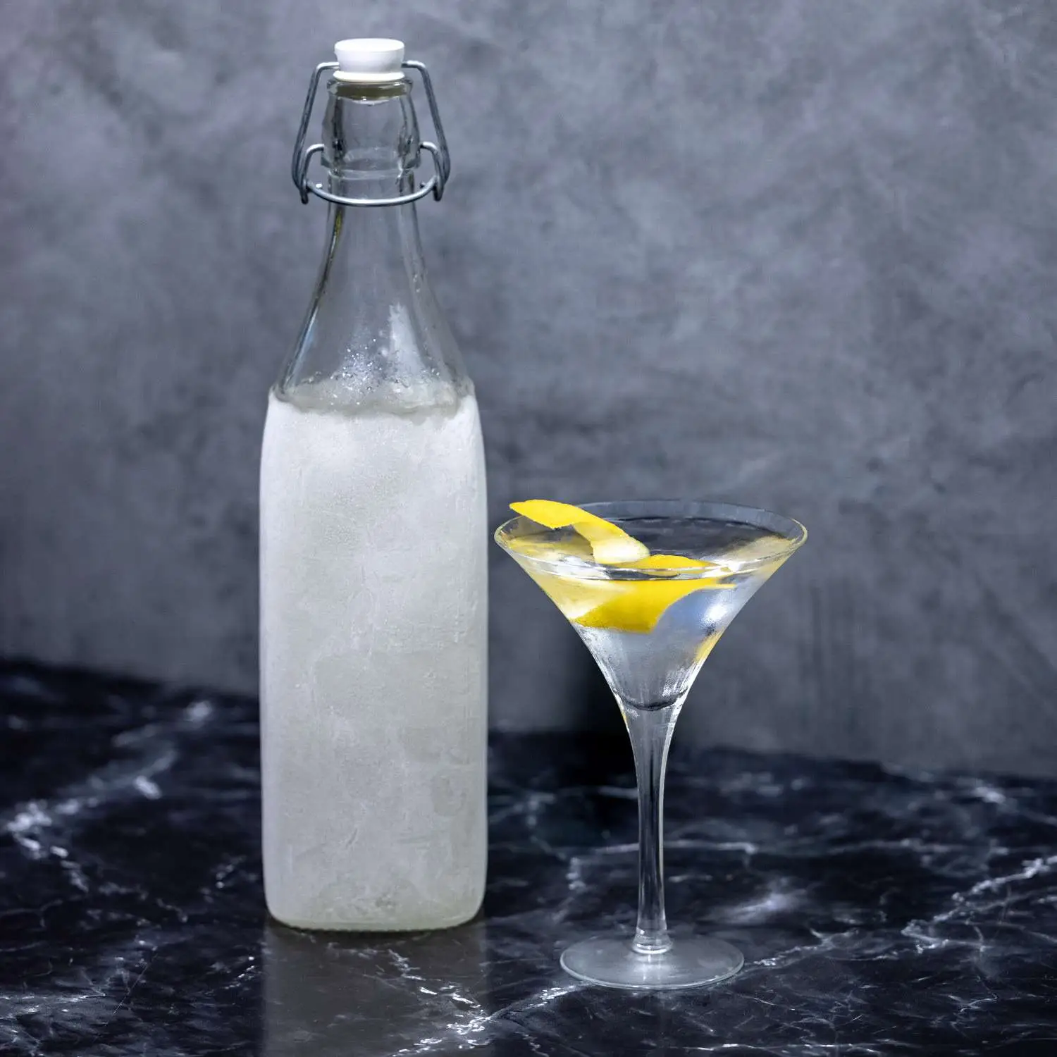 A frozen flip-top bottle filled with gin, standing next to a v-shaped Martini glass showing a Dukes Martini with a lemon twist