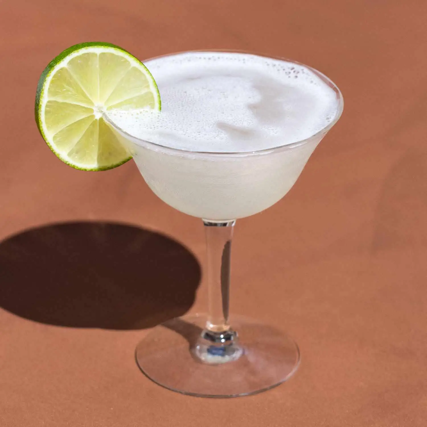 Vodka Gimlet in an etched coupe glass with lime wheel garnish, on brown background