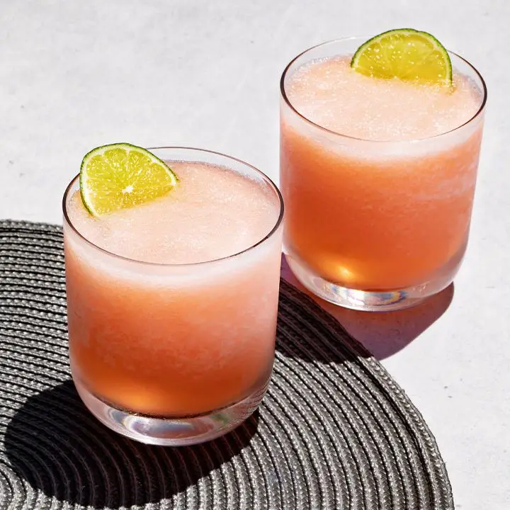 two Pink Frozen Margaritas in rocks glasses with lime wheels poking out of their tops