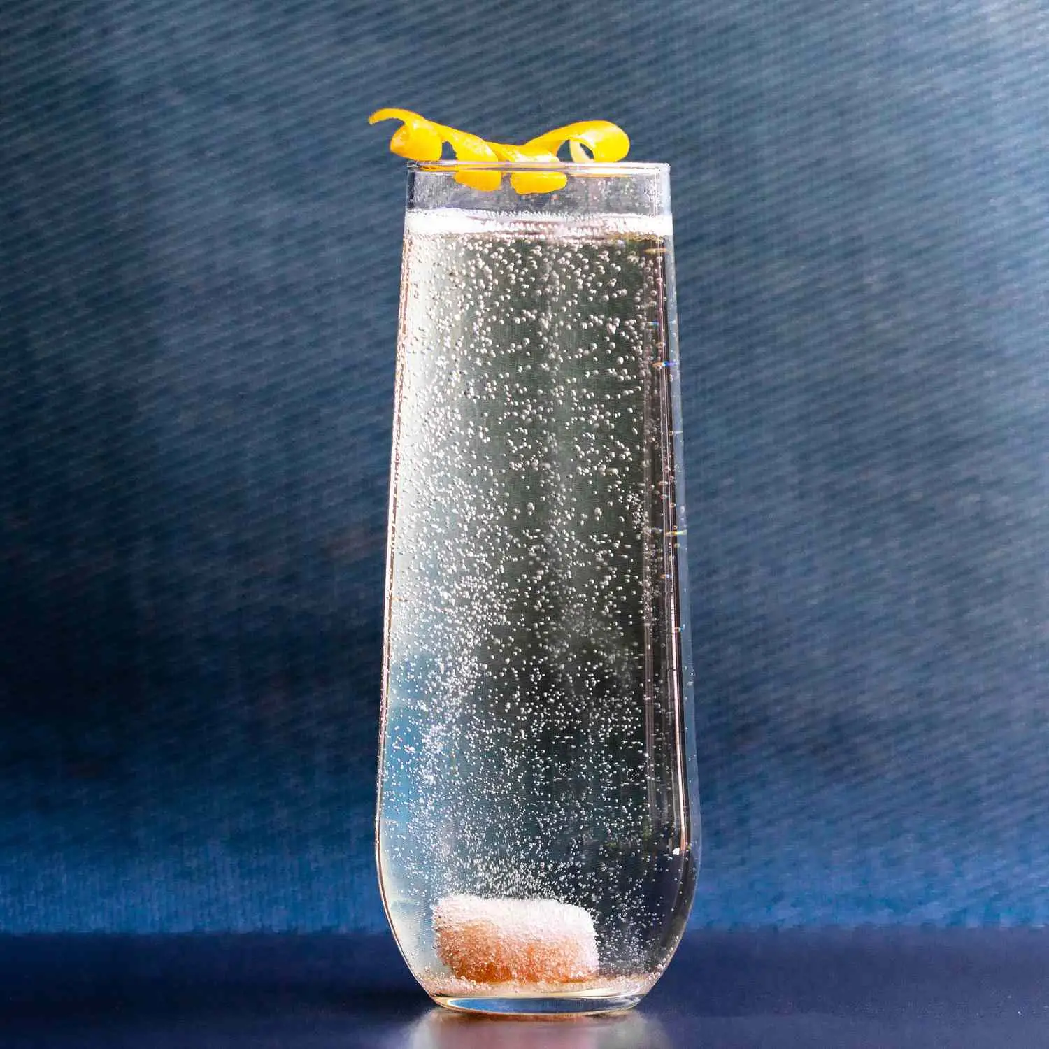 Champaign Cocktail in highball glass, with sugar cube bubbling in the bottom, on blue background