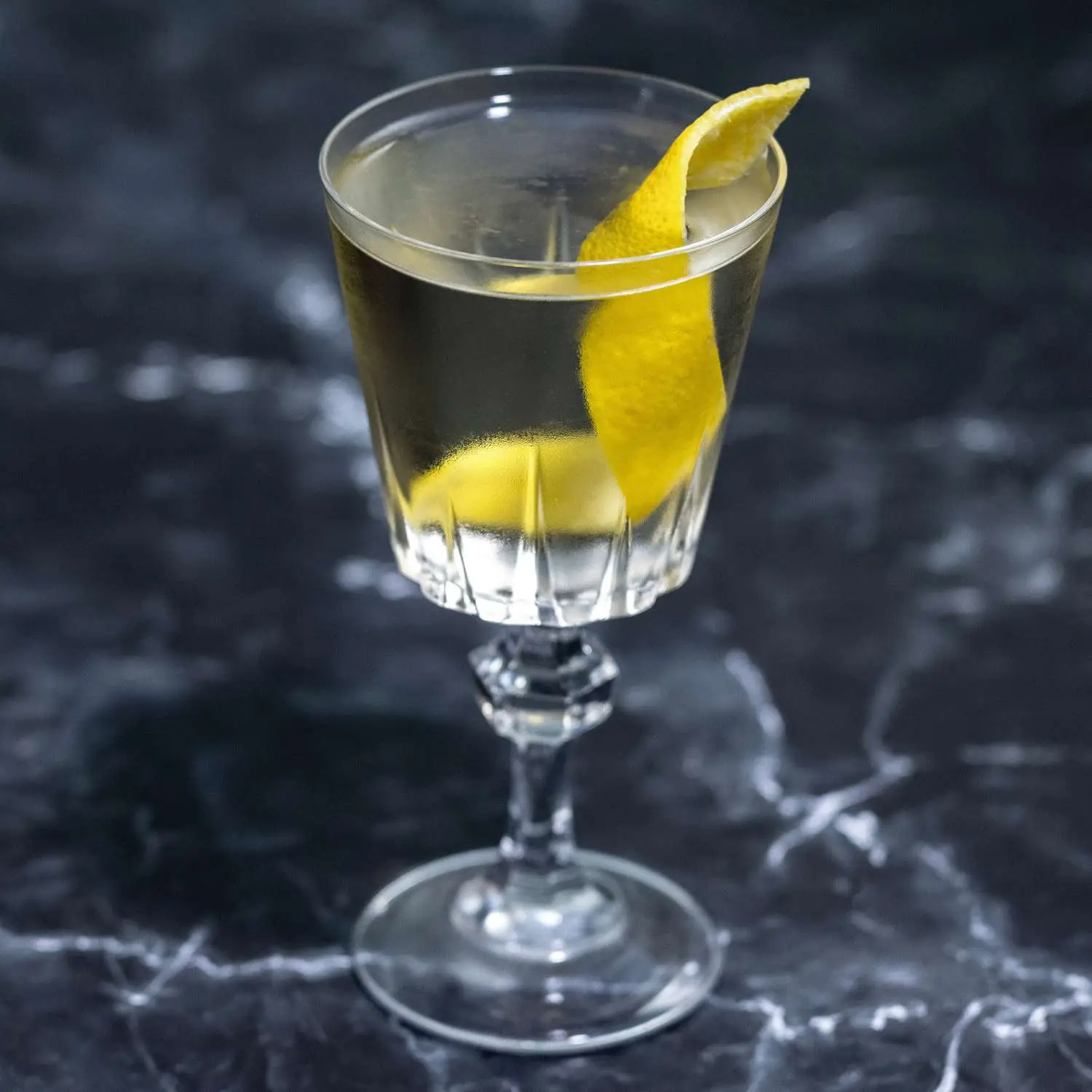 Marguerite cocktail in Nick & Nora glass with thick twist of lemon peel as garnish, placed on dark marble background