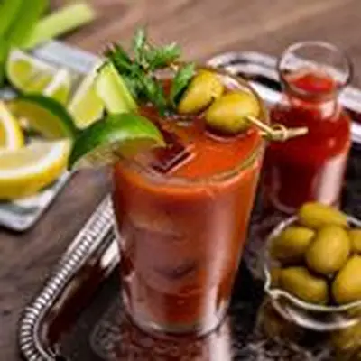 Bloody Mary in pint glass garnished with limes, parsley and olives, on silver tray surrounded by other garnishes
