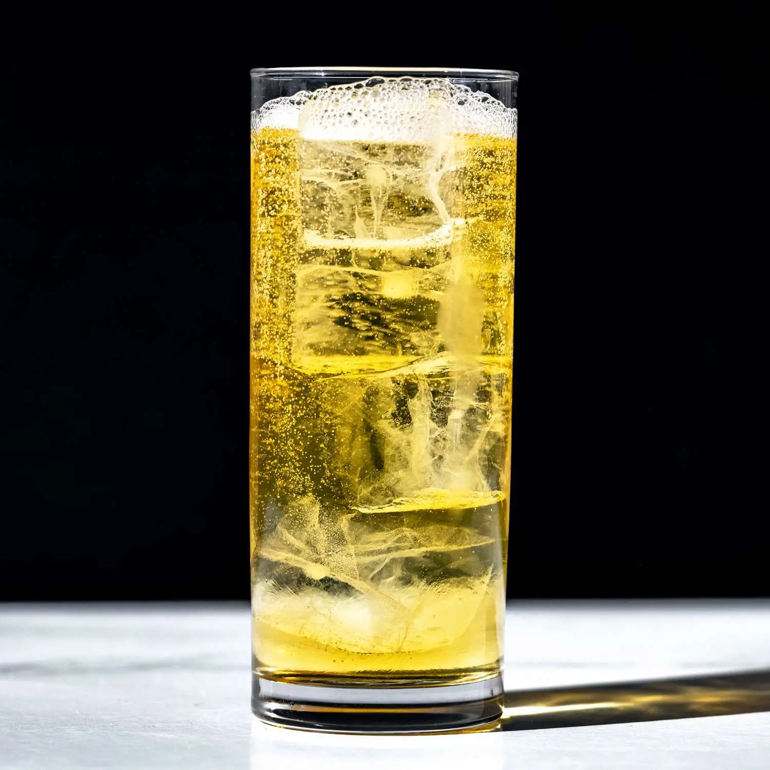 Golden-hued Whiskey Highball in tall highball glass with carbonated bubbles rising, on dark solid background