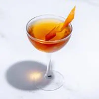 Overhead-angled view of a Martinez cocktail in a coupe class on white marbled background, with orange twist along the rim