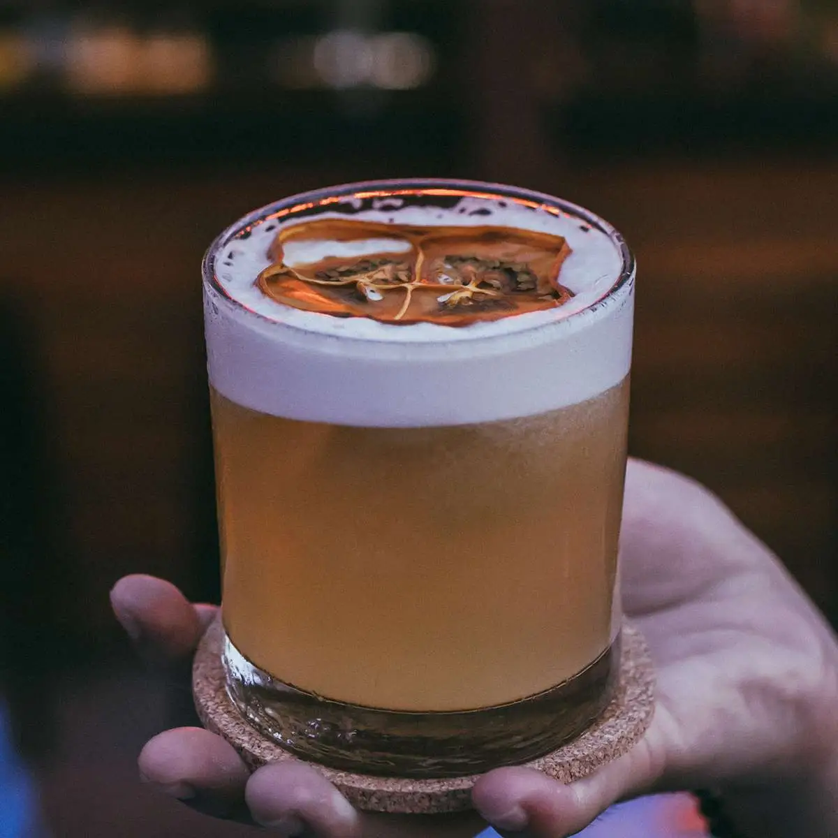 Hand holding Petronio sour cocktail in rocks glass with dehydrated orange peel