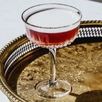 Reddish-hued French Martini in silver-rimmed coup glass, on bronze tray