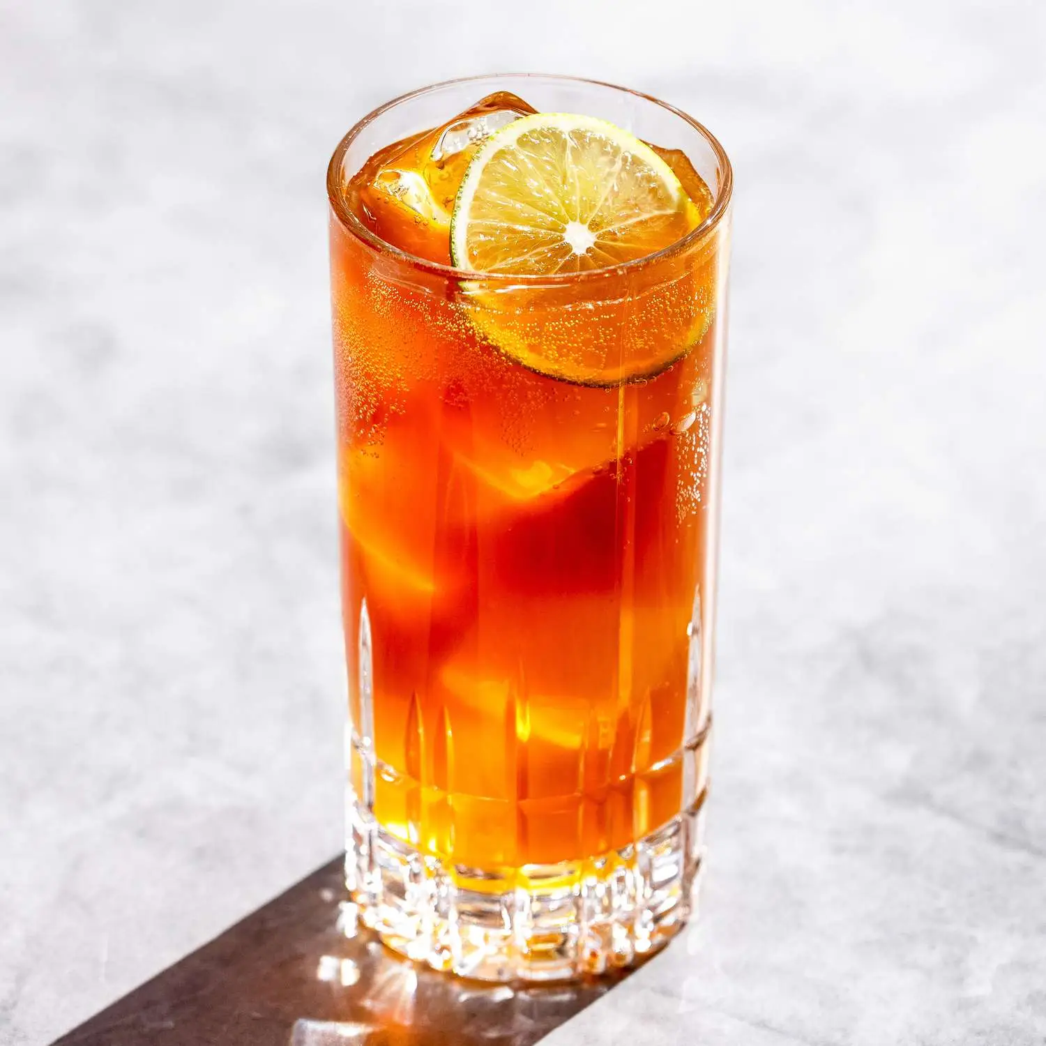 Dark and Stormy cocktail in a highball glass with lime wheel on top, photographed on light marble background