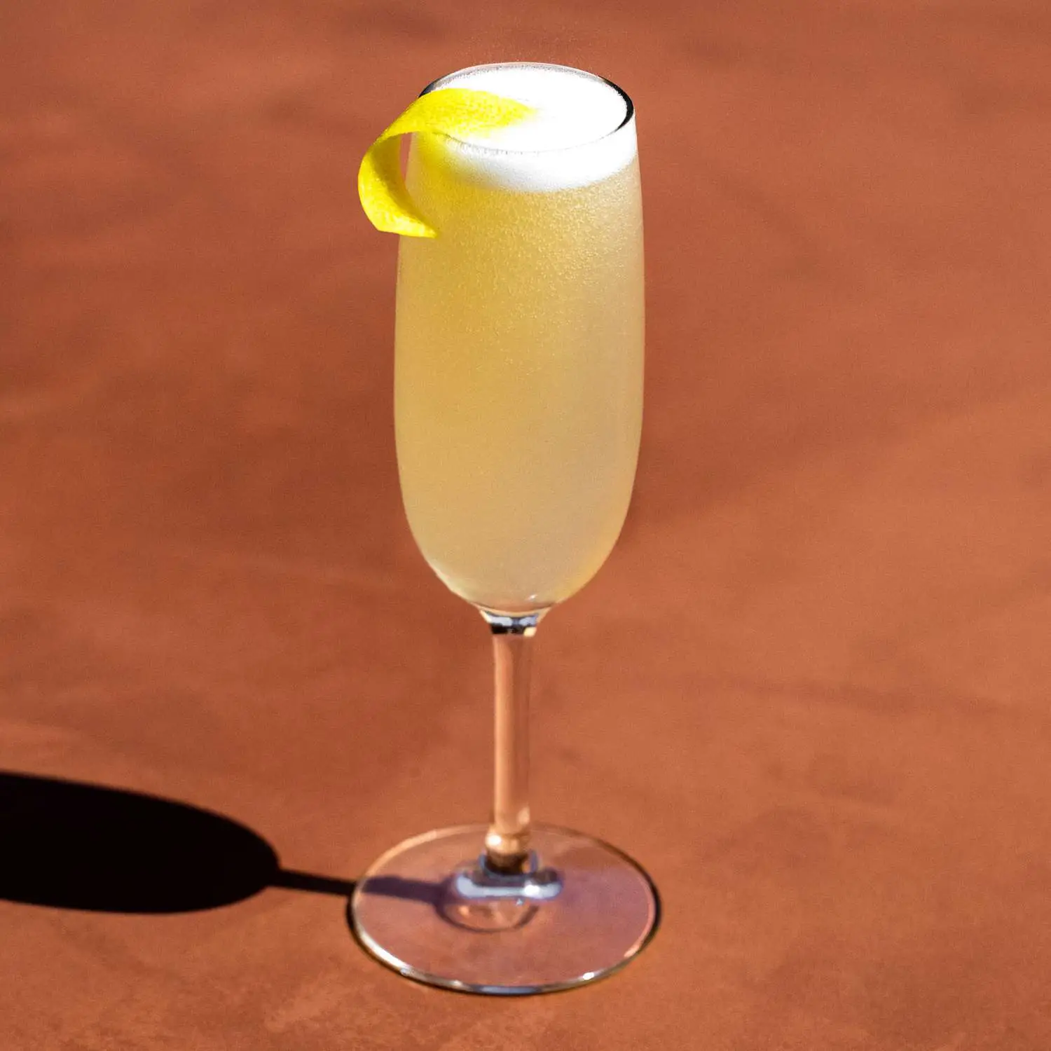 French 75 in Champagne flute with lemon twist garnish and bubbles, on dark tan background