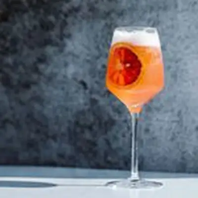 Off-centered Colletti Royale pink bubbly spritz cocktail served in wine glass with blood orange wheel, shot on marble surface against gray background 