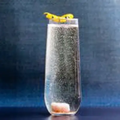 Champaign Cocktail in highball glass, with sugar cube bubbling in the bottom, on blue background
