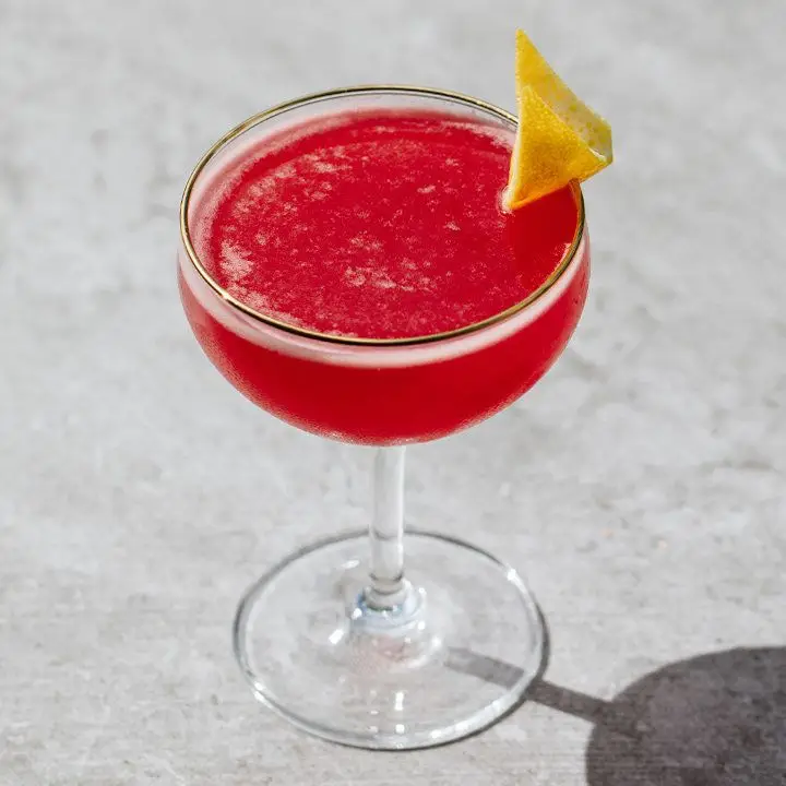 deep-red bebbo cocktail in a coupe, garnished with a lemon twist and served on a gray surface