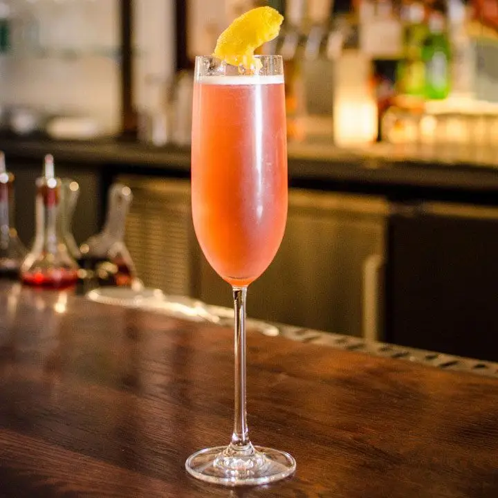 Mrs. Robinson cocktail in a flute with a lemon peel garnished, served on a wooden bar