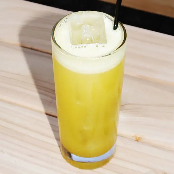 yellow-colored Delhi Cooler cocktail in a Collins glass, served over ice with a black straw
